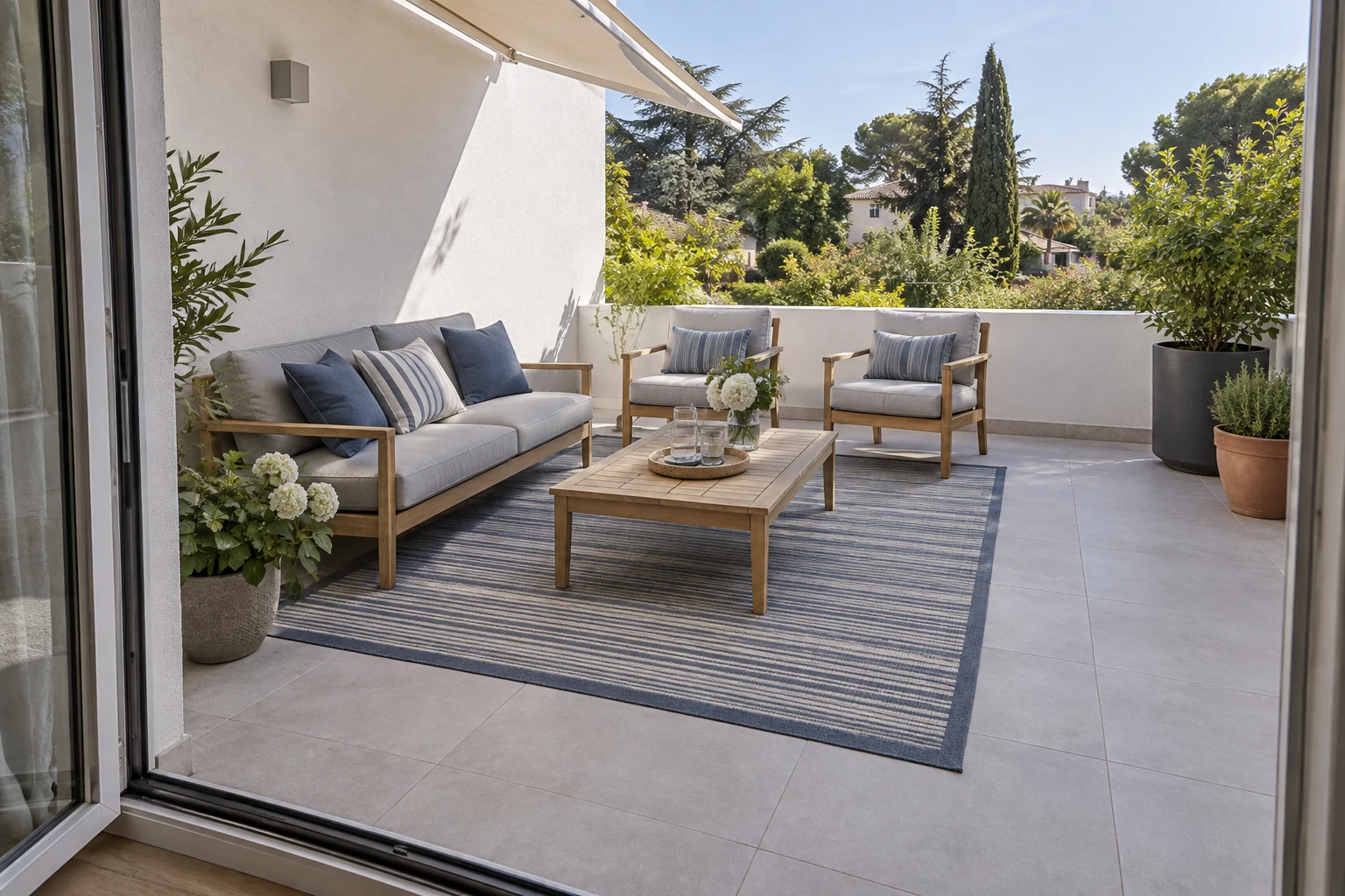 Salon de terrasse avec canapé, fauteuils, tapis extérieur et végétation